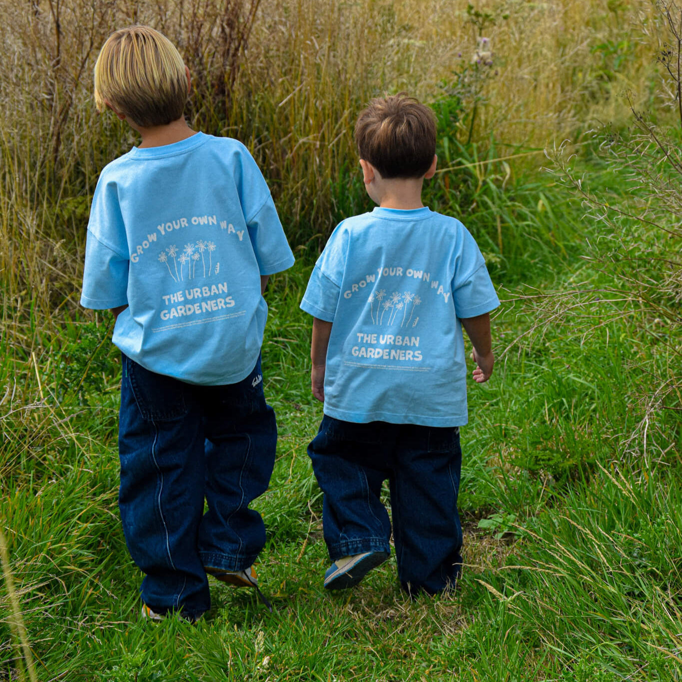 Two kids wearing oversized "GYOW - Oversized Tee" walking in grass, playful design, Toddie brand.