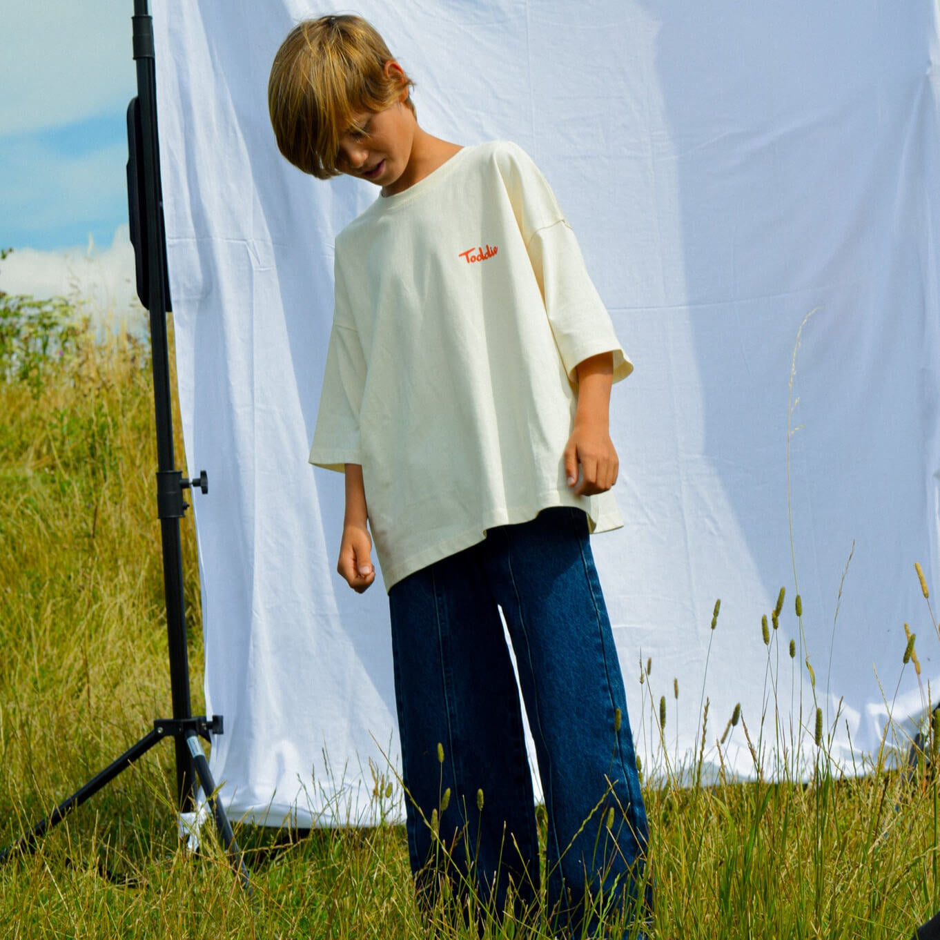 Child wearing Balloon styled - Denim Jeans with oversized white shirt standing outdoors on grass