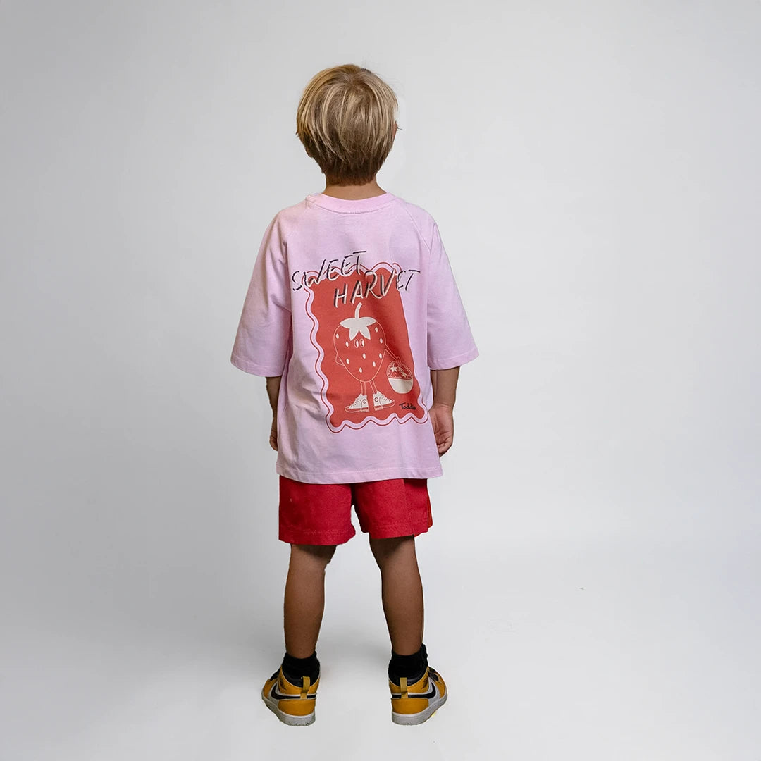 Sweet Harvest - Oversized Tee Pink featuring playful strawberry graphic worn by child from back view
