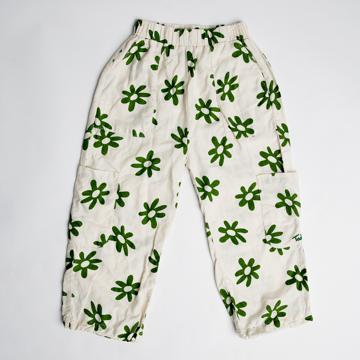 Cargo Flower Pants in white with green flower print, relaxed fit, side pockets, and adjustable hems for kids.