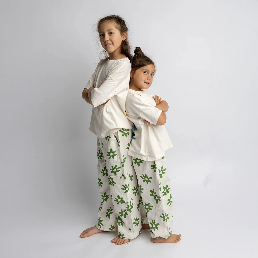 Two kids wearing relaxed fit Cargo Flower Pants with green floral prints standing back to back.