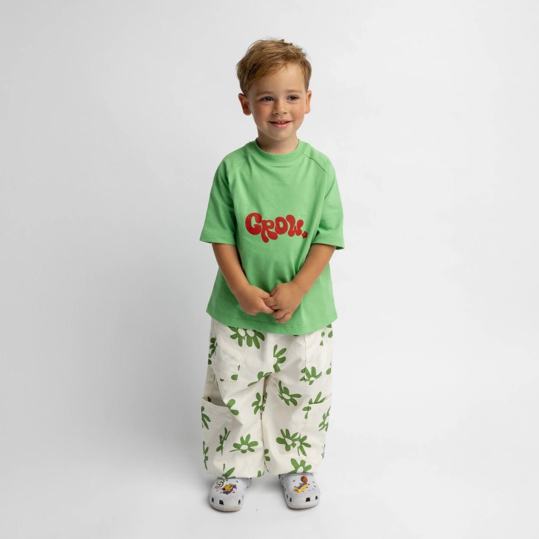 Child wearing green Grow - Oversized Tee with red lettering, paired with white pants with green leaf patterns.