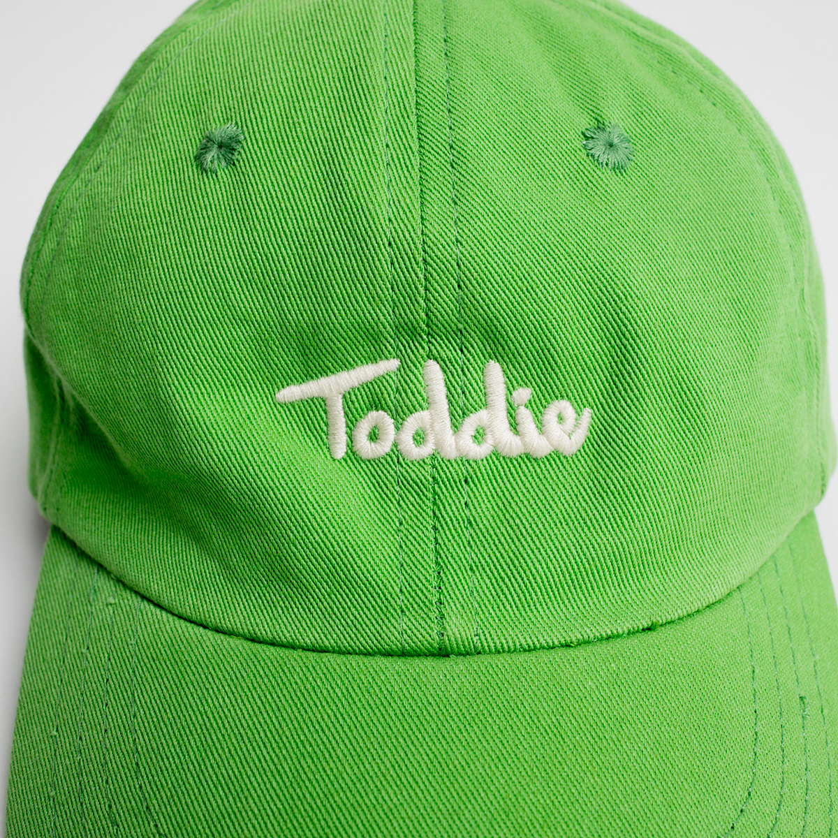 Bright green Toddie Cap with white embroidered logo, designed for comfort and durability for active kids.