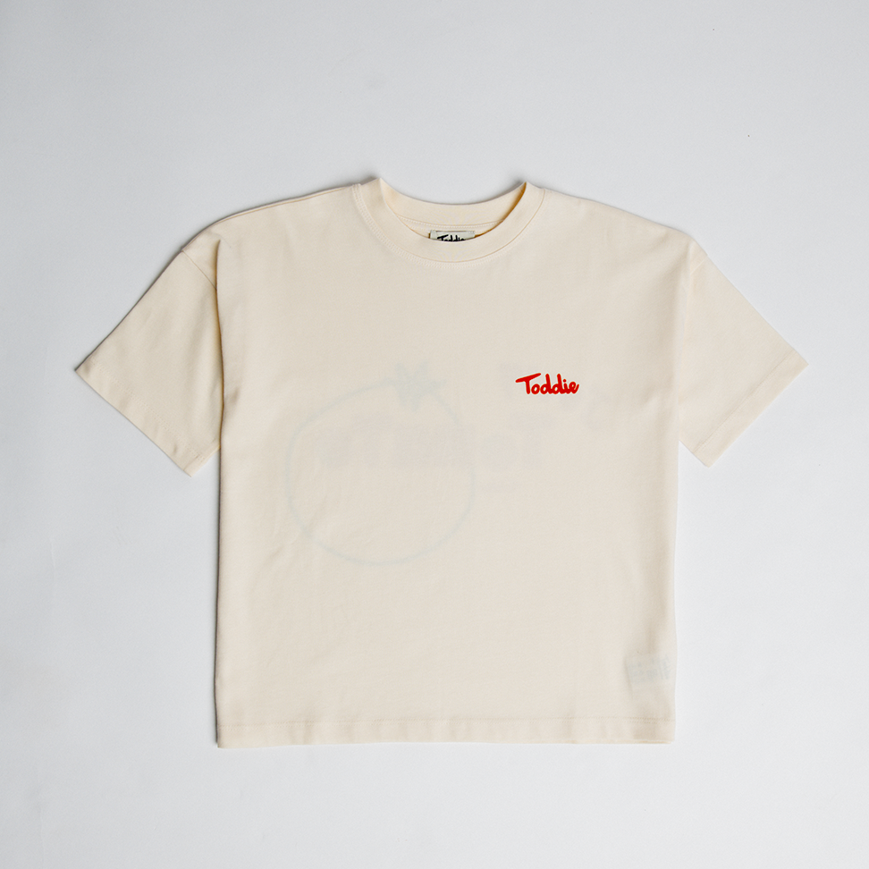 Juicy Tomato - Oversized Tee in cream with small red logo on front and faint tomato graphic on back, soft cotton material.