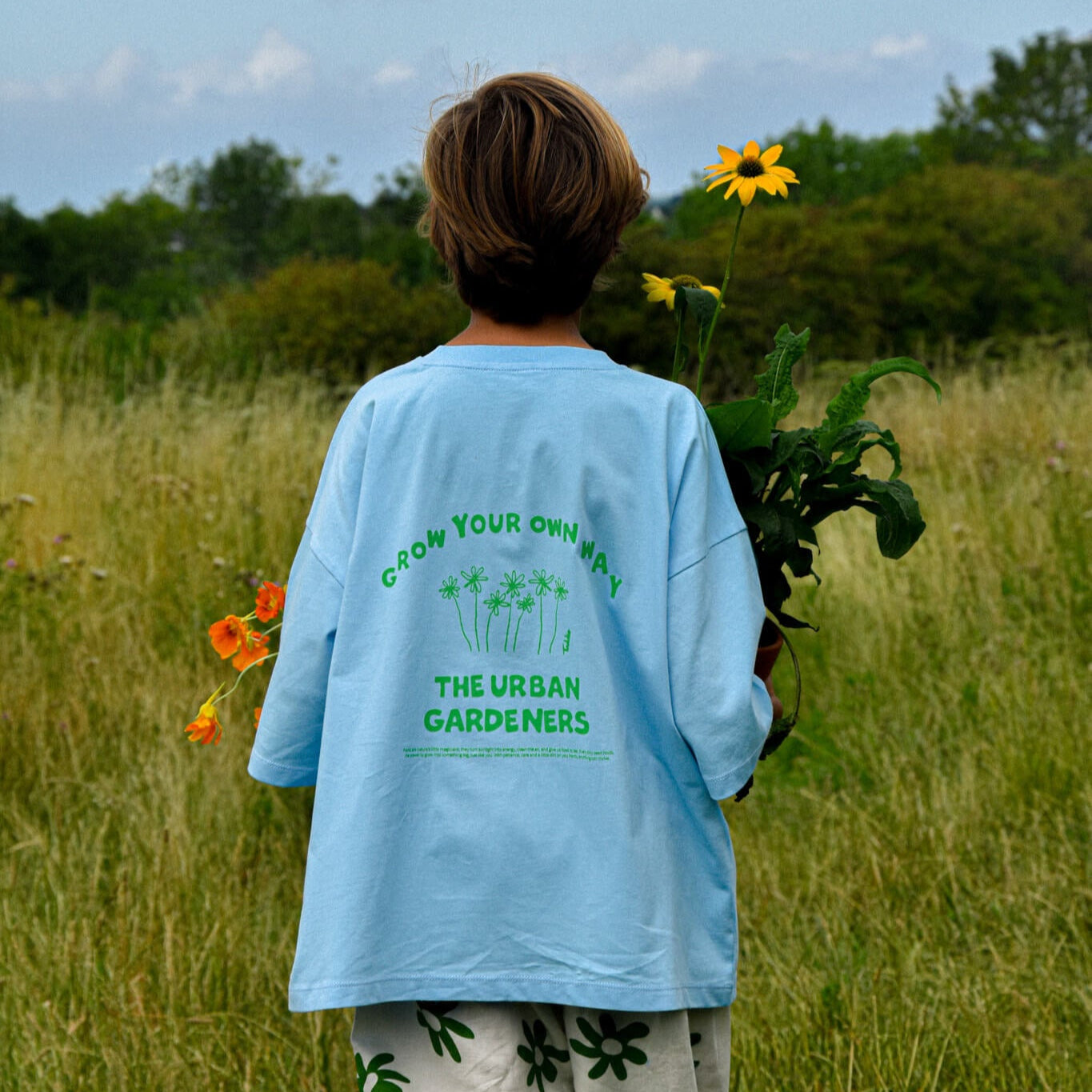 Child wearing oversized GYOW - Oversized Tee with "Grow Your Own Way" design holding flowers, Toddie brand.