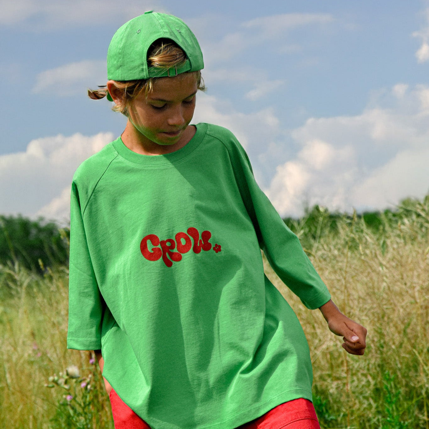 Child wearing green oversized Grow - Oversized Tee with red lettering playing outdoors on a sunny day