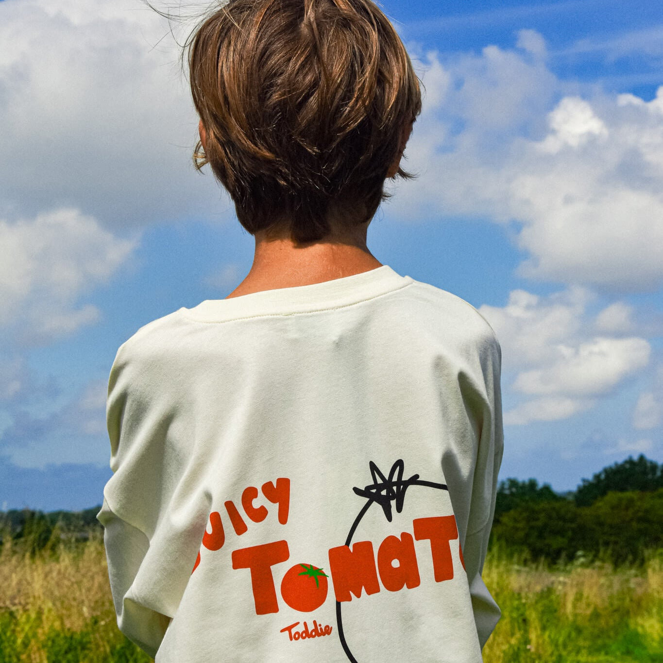 Child wearing Juicy Tomato - Oversized Tee with bold tomato graphic on back in outdoor setting.