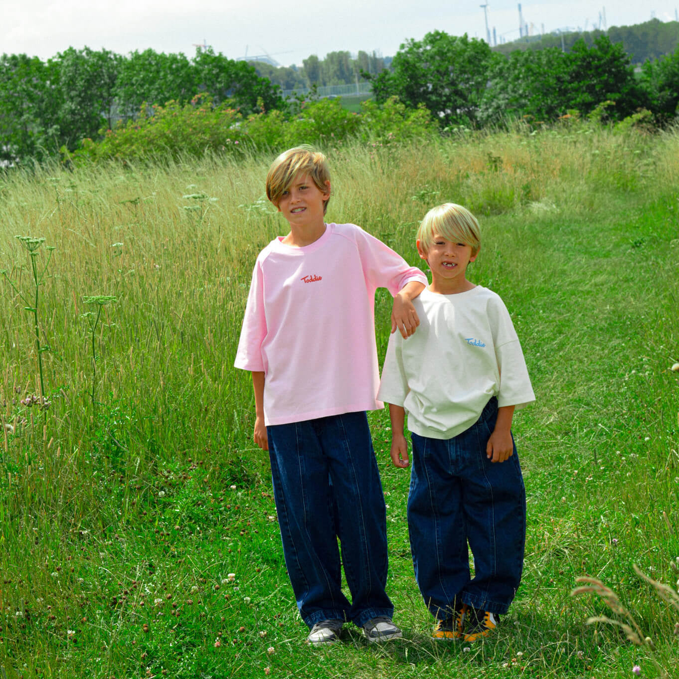 Two boys wearing Sweet Harvest - Oversized Tee Pink and white tees standing in a grassy field outdoors.