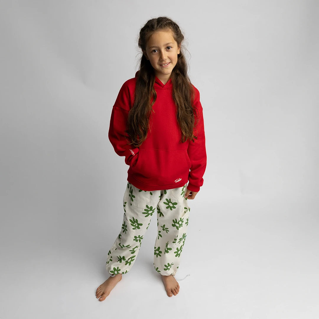 Child wearing WMB - Oversized Hoodie Red with white pants featuring green floral prints on a neutral background.