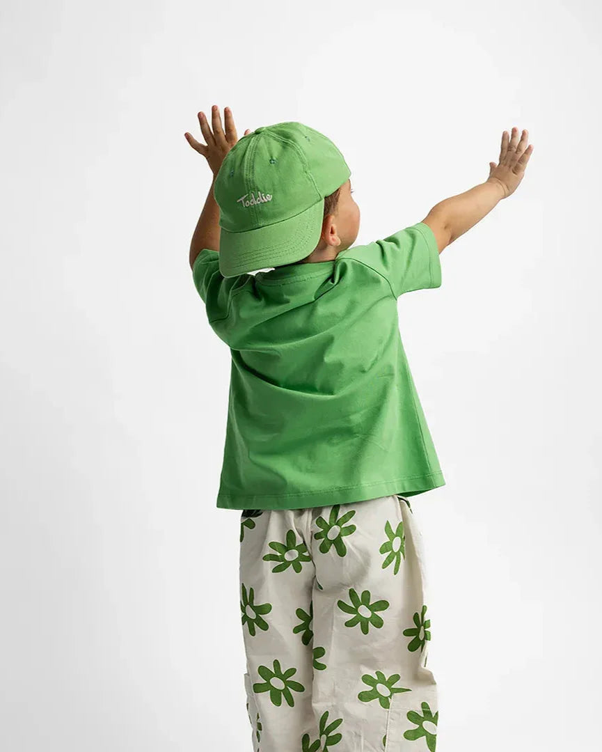 Child wearing a vibrant green Toddie Cap with embroidered logo and matching green shirt and floral pants.
