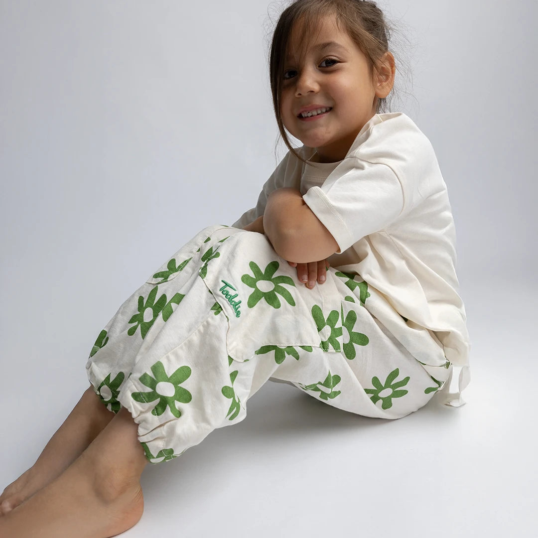Child wearing relaxed fit Cargo Flower Pants with green floral print and adjustable hems sitting and smiling