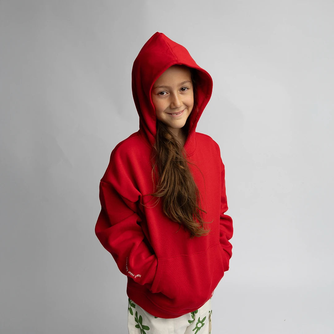 Child wearing a cozy red hoodie with oversized fit and hood, "WMB - Oversized Hoodie Red" visible on sleeve.